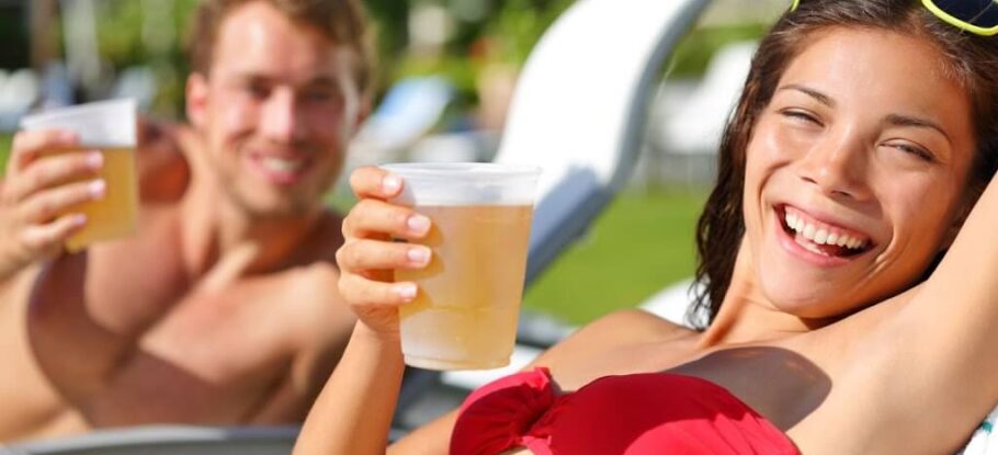 man and woman smiling on lounge chairs while holding beers