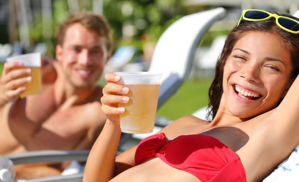 man and woman smiling on lounge chairs while holding beers