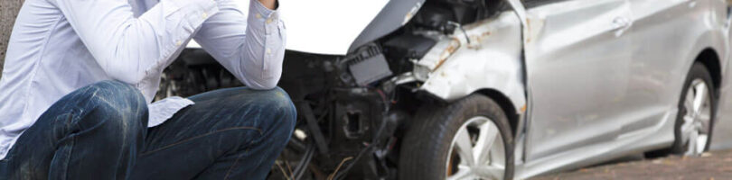 man in pain after car accident; totaled car in background
