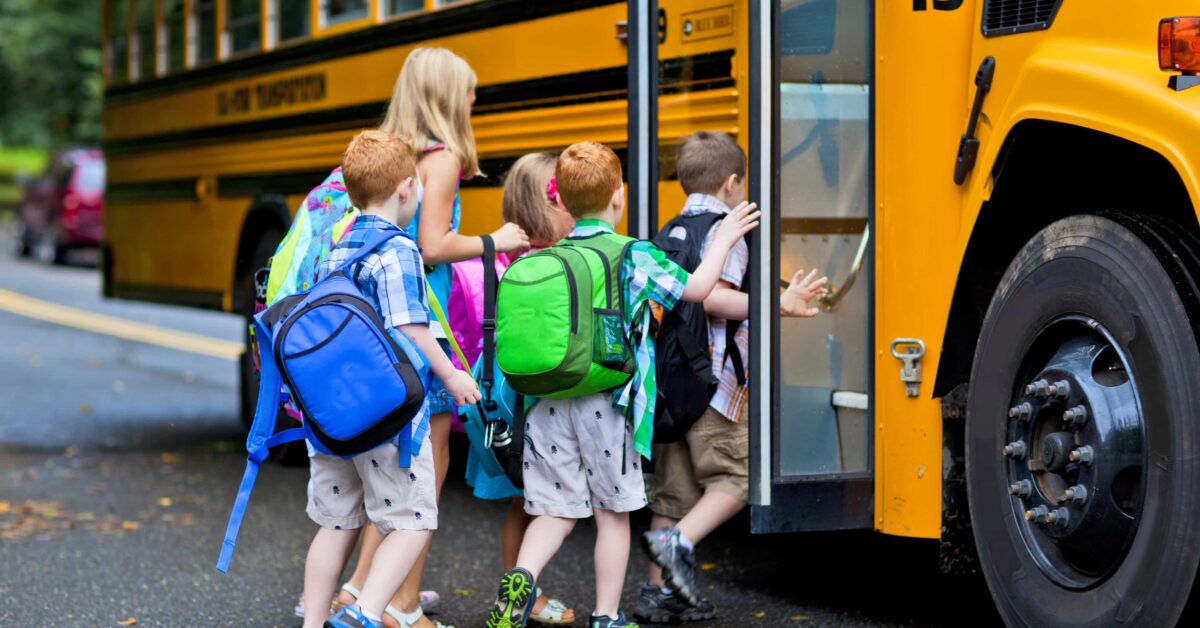 women walking school children onto school bus on a neighborhood road