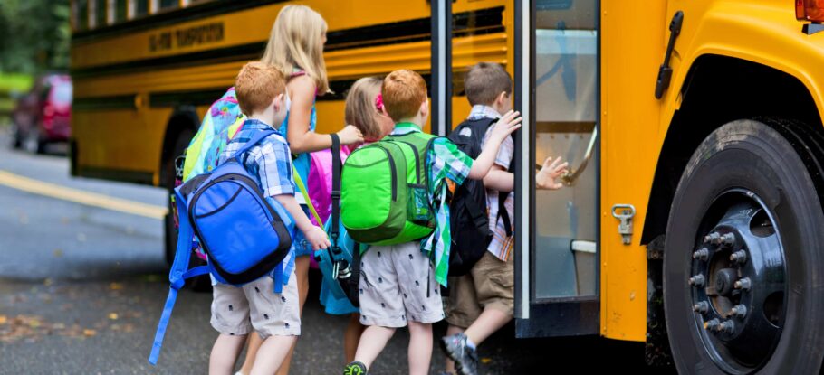 women walking school children onto school bus on a neighborhood road