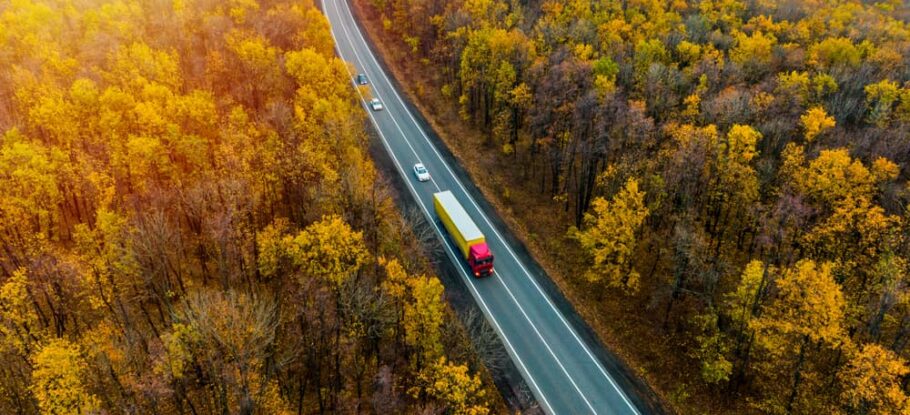 fall scene with orange and red leaves, highway in the middle of woods with a tractor-trailer and two