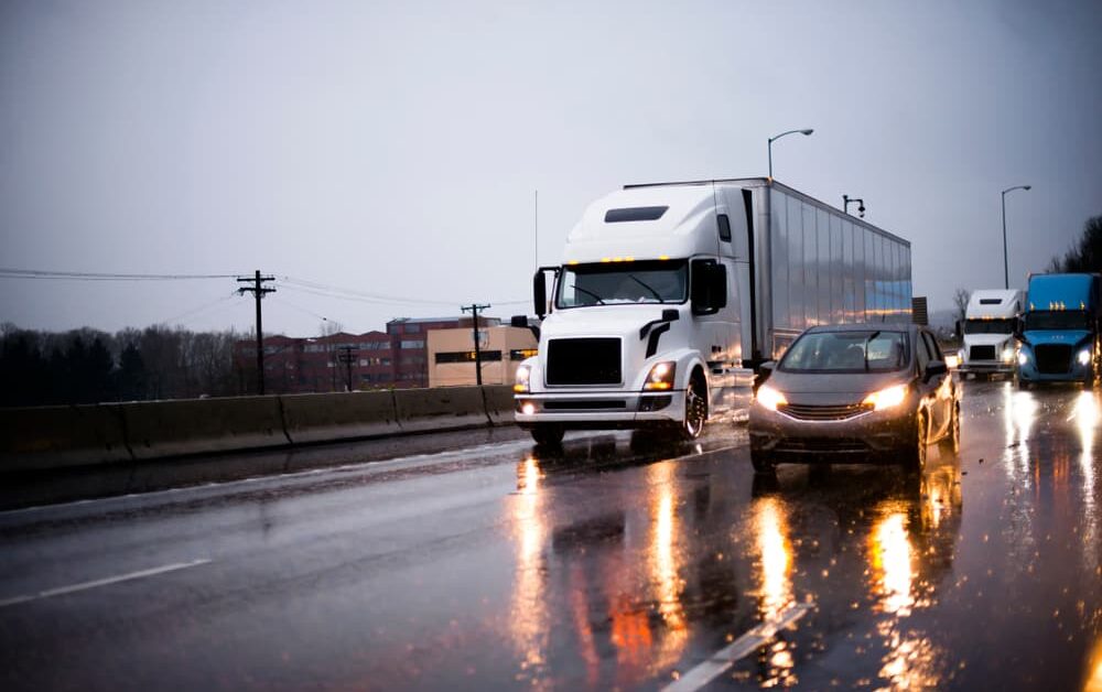 car riding beside 18-wheeler on wet highway due to rain