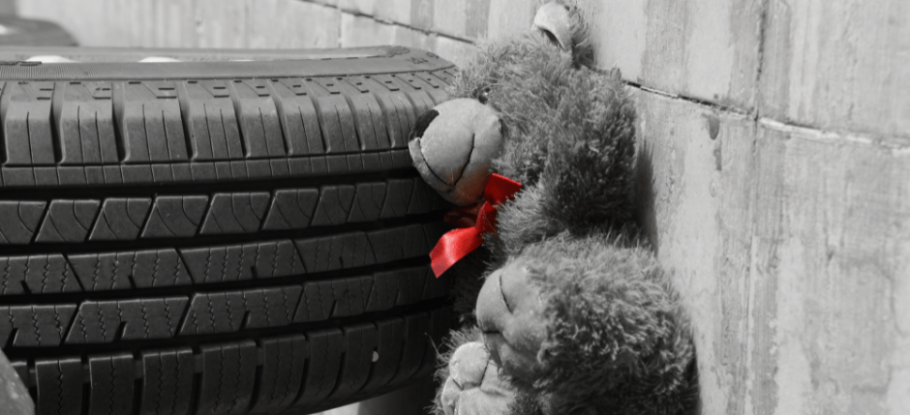 childs teddy bear in front of a car wheel