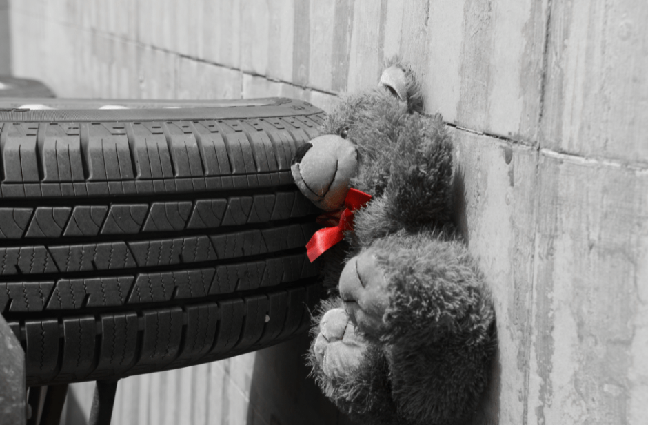 childs teddy bear in front of a car wheel
