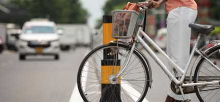 Mujer esperando cruzar una calle con su bicicleta, quien podría necesitar un abogado de accidentes en bicicleta.
