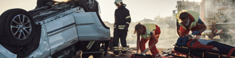 car flipped upside down on road with paramedics on scene following a fatal truck accident